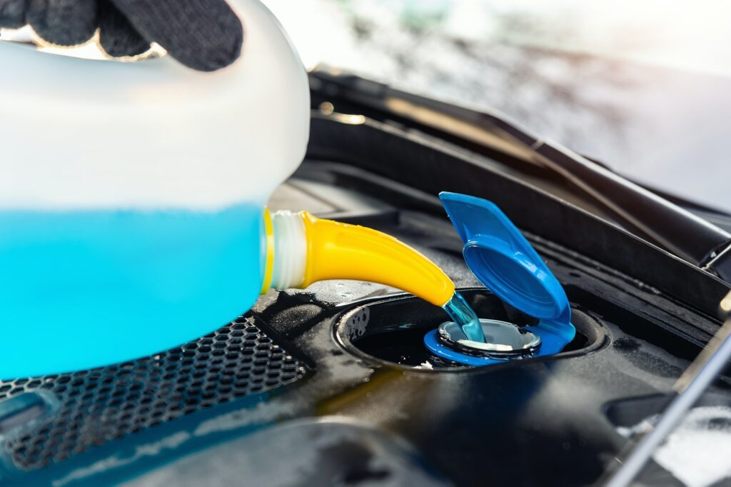 driver hand in gloves pouring blue antifreeze liquid for winter car windshield screen washing