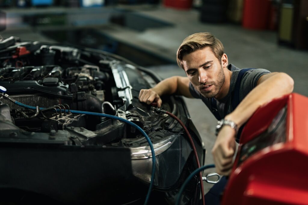 Young mechanic maintaining AC unit of a car at auto repair shop.